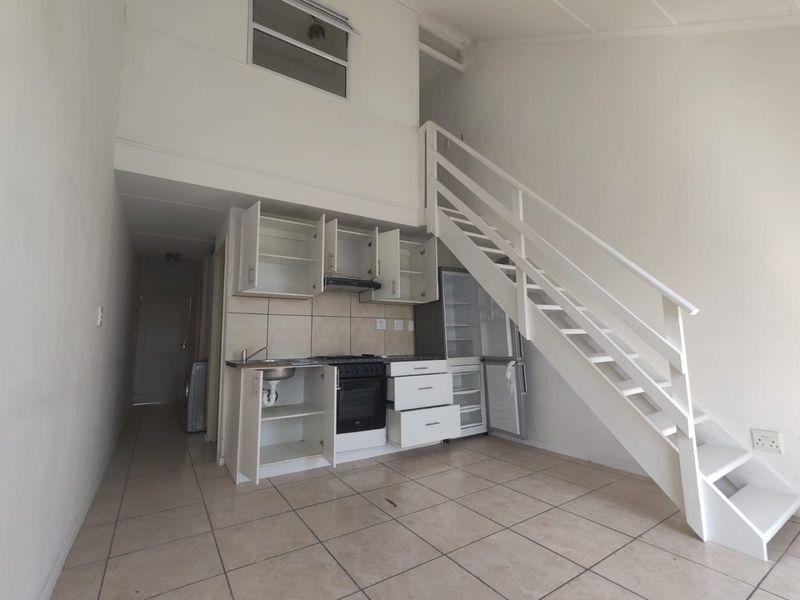 Open-plan living area featuring a compact kitchen with built-in cabinetry, oven, and extractor fan, complemented by a staircase leading to a mezzanine level.