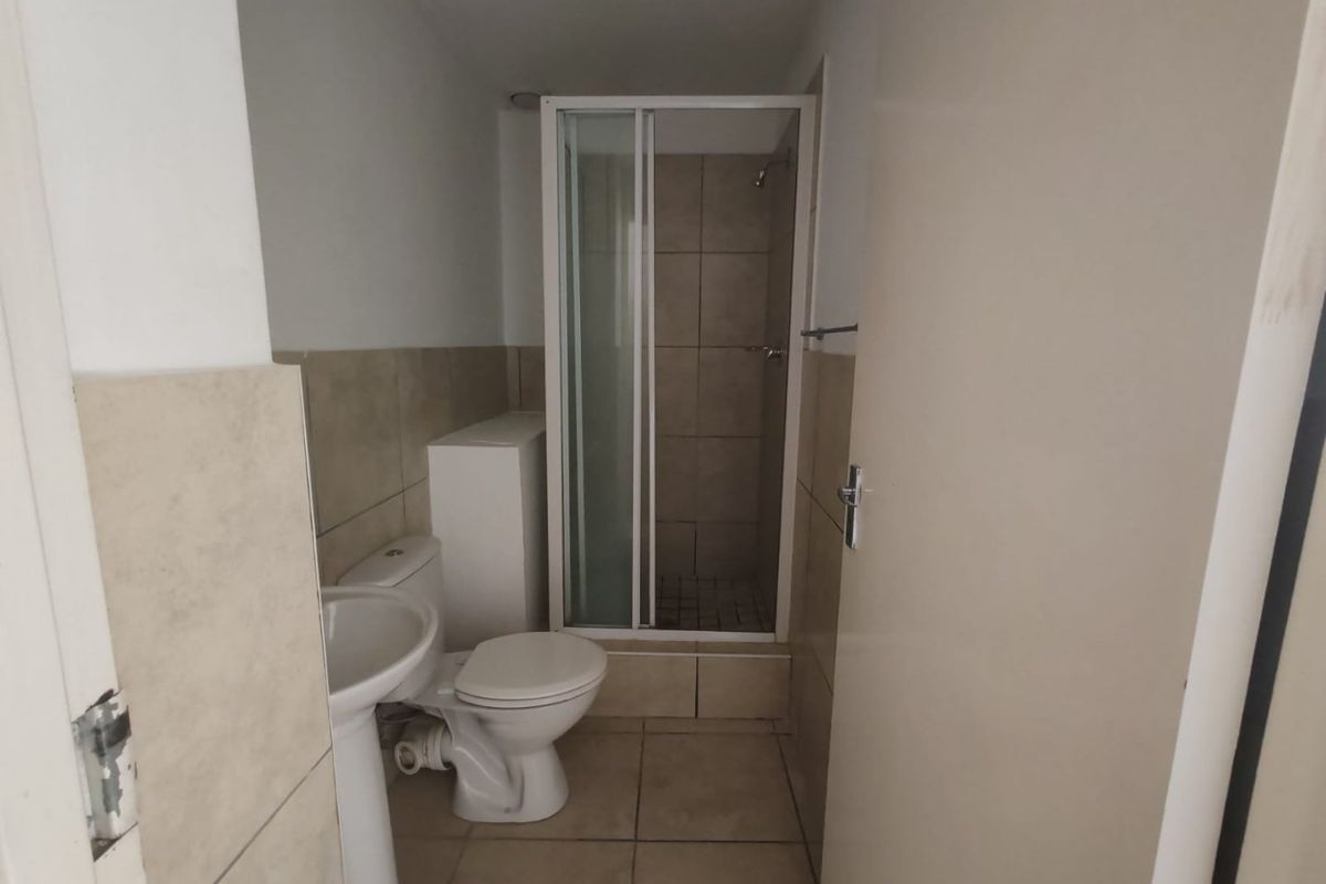 A functional bathroom featuring a shower enclosure, pedestal basin, and toilet with neutral wall and floor tiling.