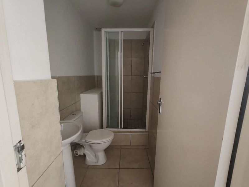 A functional bathroom featuring a shower enclosure, pedestal basin, and toilet with neutral wall and floor tiling.
