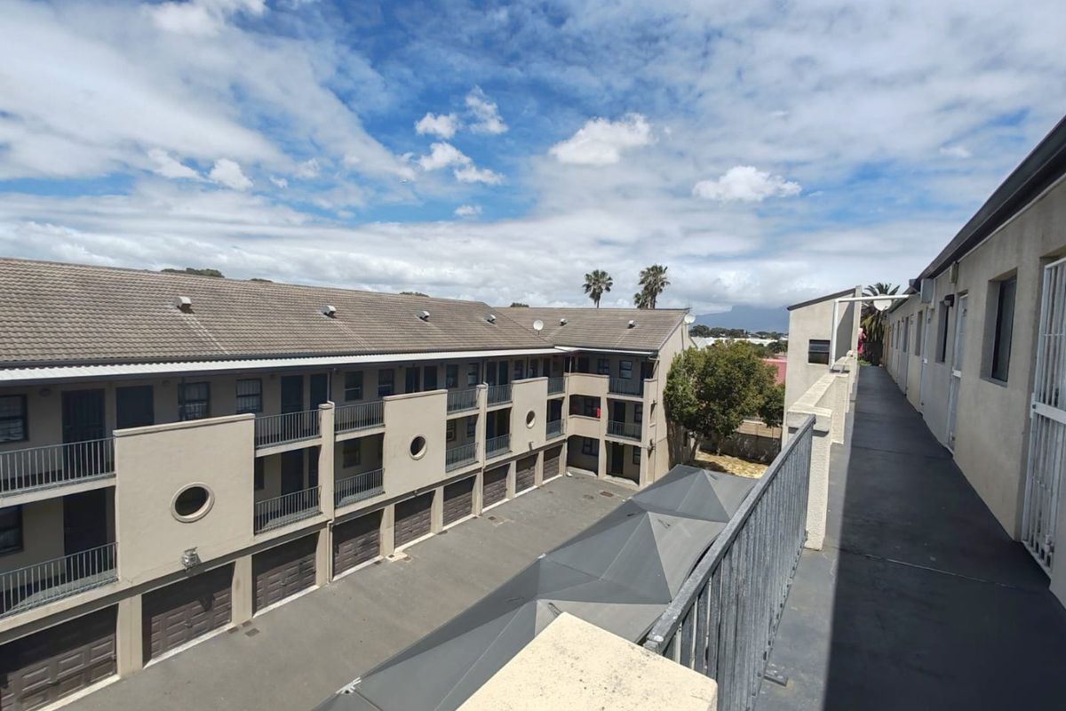 An elevated view of the apartment complex courtyard, featuring a communal walkway, metal balustrades, and ground-level garage access.