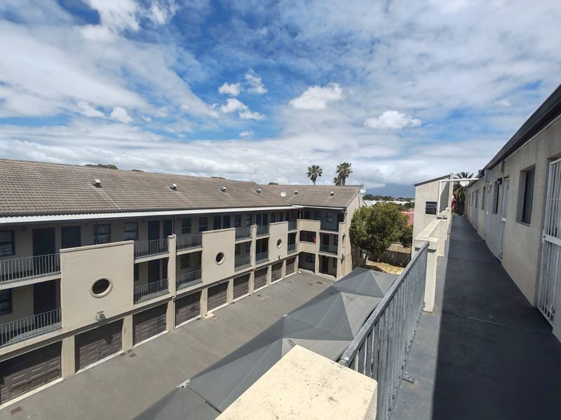 An elevated view of the apartment complex courtyard, featuring a communal walkway, metal balustrades, and ground-level garage access.