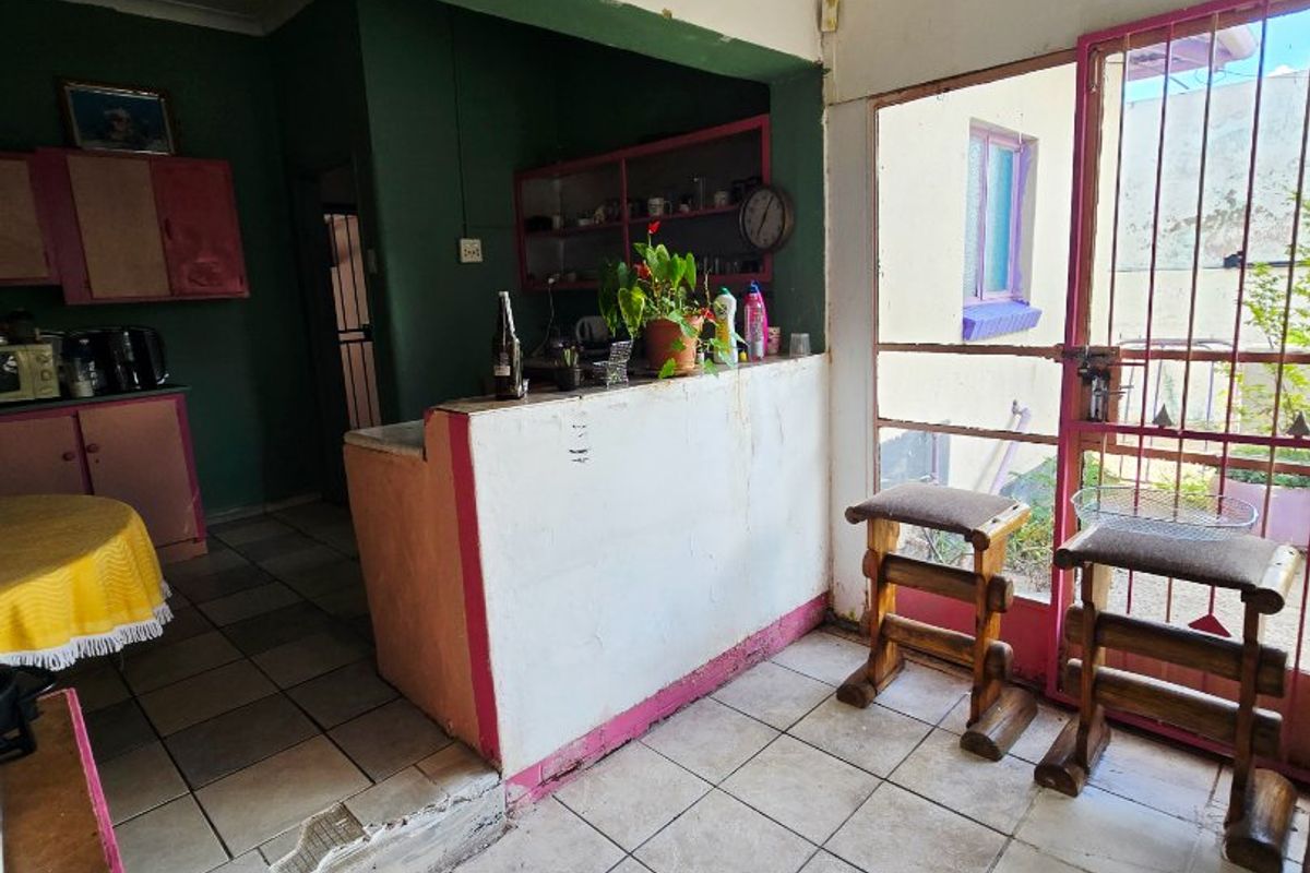 A dated kitchen area featuring tiled flooring, built-in cabinetry, and a breakfast bar, requiring cosmetic updates and repairs to the floor edge.