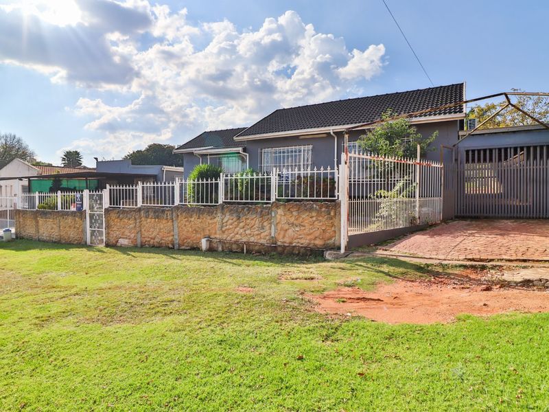 Front exterior view of a detached house featuring a stone boundary wall, metal security fencing, and a paved driveway leading to a garage structure.