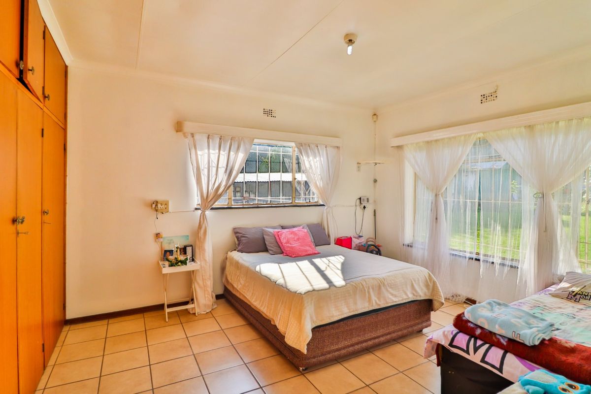 A bedroom featuring tiled flooring, built-in wooden wardrobes, and large windows with security bars, providing natural light and garden views.
