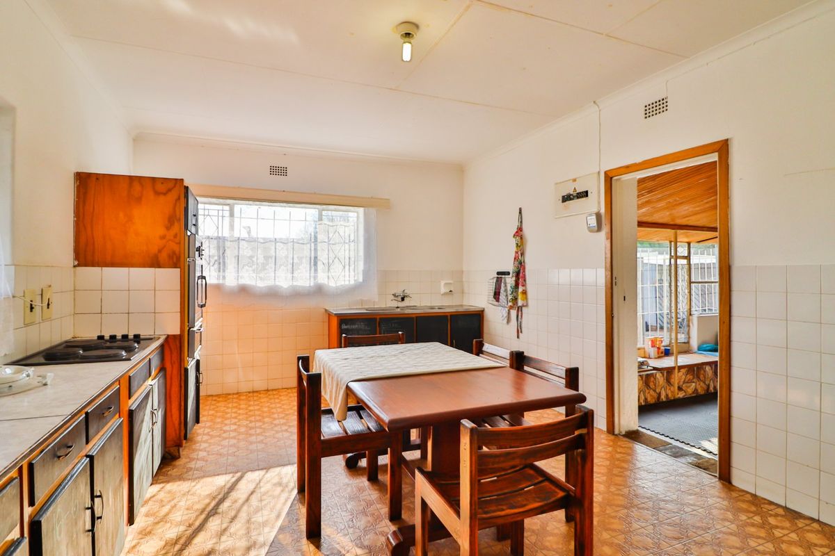 A dated kitchen featuring original cabinetry, tiled splashbacks, and vinyl flooring, offering a functional layout with potential for modernization.