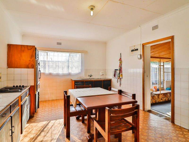 A dated kitchen featuring original cabinetry, tiled splashbacks, and vinyl flooring, offering a functional layout with potential for modernization.