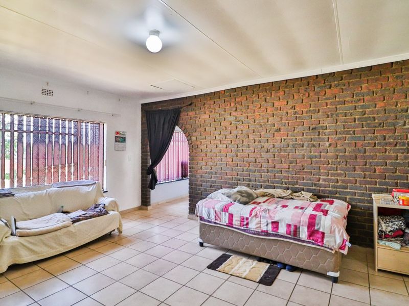 Spacious living area featuring a prominent exposed brick feature wall, tiled flooring, and an arched entryway leading to an adjacent space.