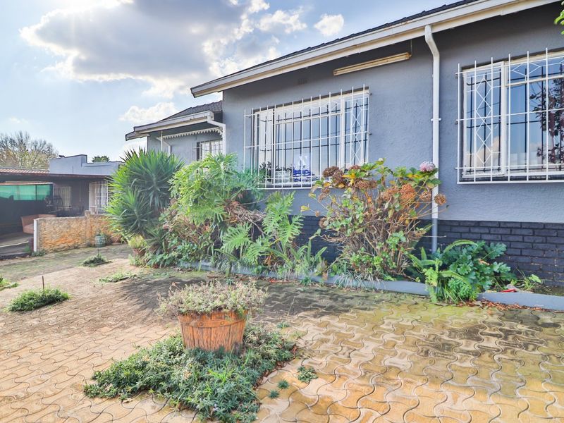 Front exterior view of the house featuring a paved driveway, security bars on windows, and established garden beds along the building facade.