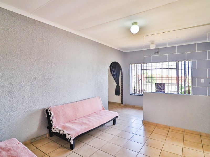 A living area featuring tiled flooring, textured walls, and an arched doorway leading to an adjacent space, with security bars installed on the windows.