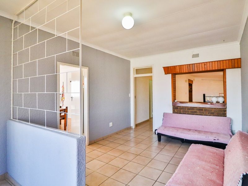 A living area featuring tiled flooring, a decorative metal room divider, and a brick-accented serving hatch connecting to the kitchen.