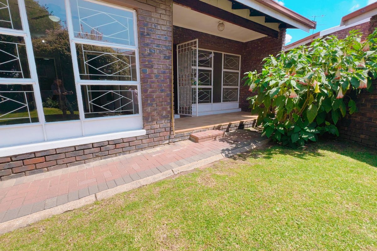 A rear view of the townhouse featuring a brick facade, a covered patio area, a paved walkway, and a well-maintained garden lawn.