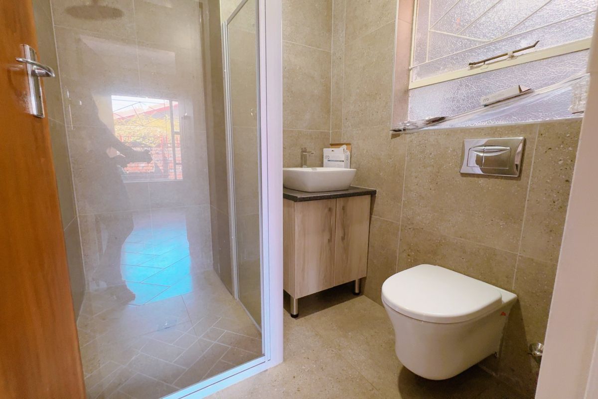 A modern, compact bathroom featuring a glass-enclosed shower, wall-mounted toilet, and a vanity with a vessel sink, finished with neutral floor-to-ceiling tiling.