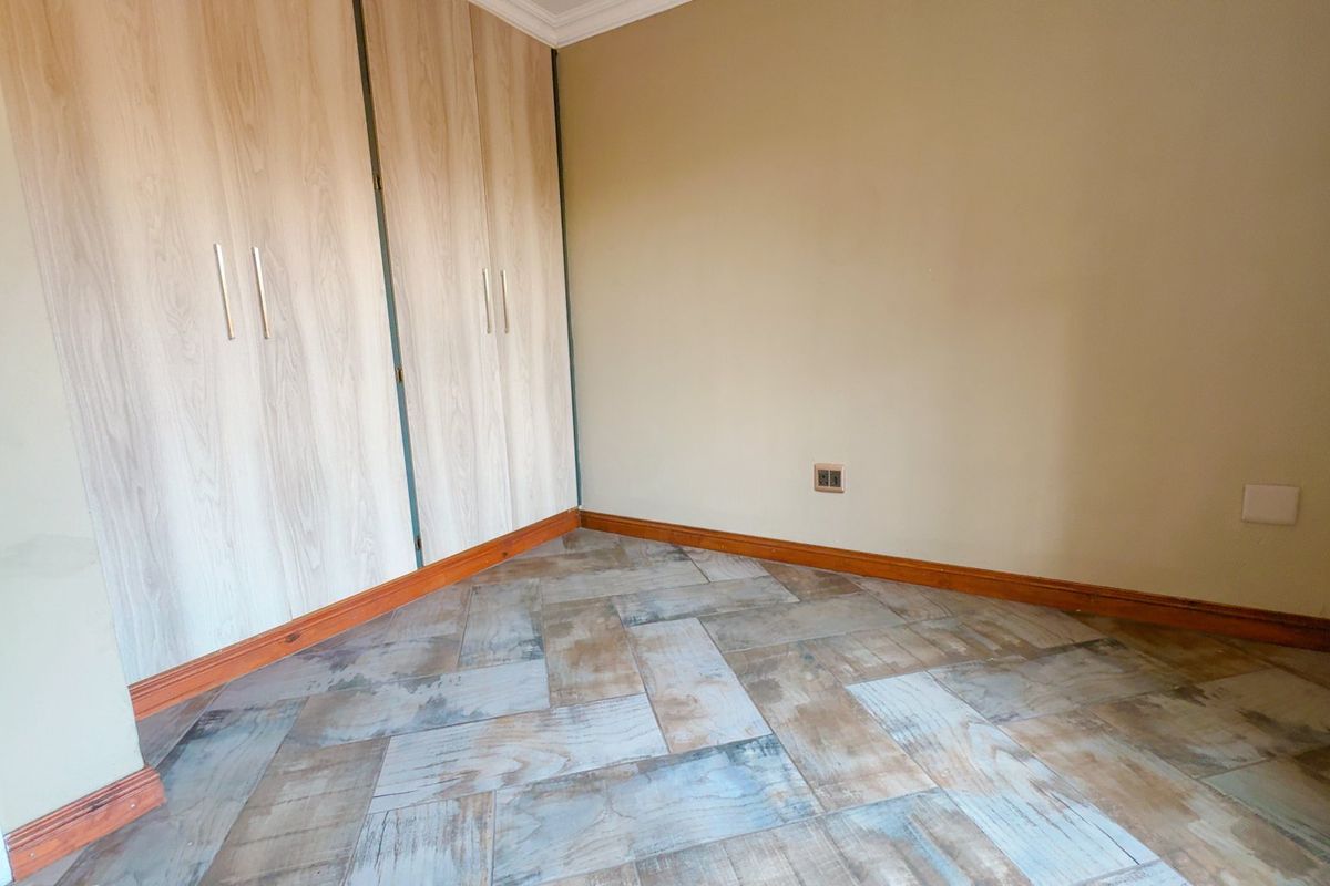 A clean, empty bedroom featuring light wood-look built-in cupboards and distinctive herringbone pattern floor tiles with neutral wall finishes.