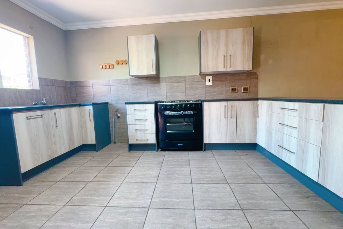 A functional kitchen featuring light wood-grain cabinetry, tiled flooring, a tiled backsplash, and a black freestanding oven, offering a clean and practical workspace.