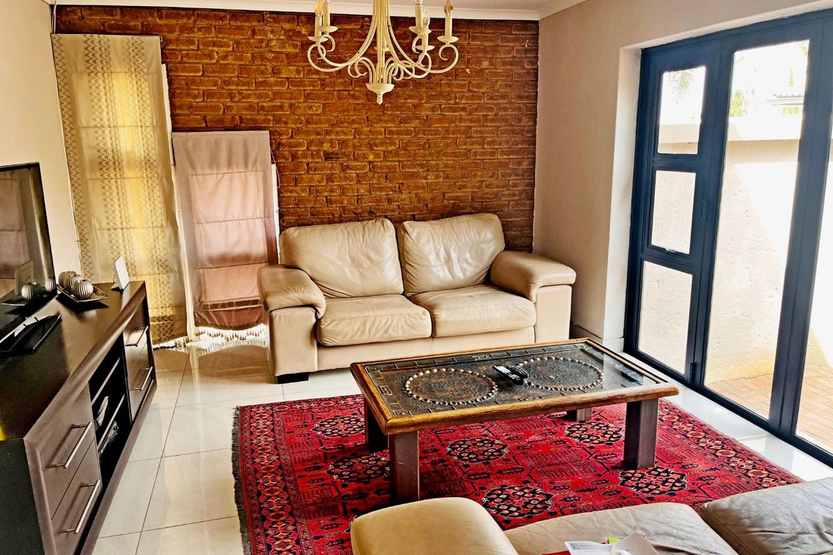 A cozy living room featuring an exposed brick feature wall, polished tile flooring, and direct access to an outdoor area through a glass door.