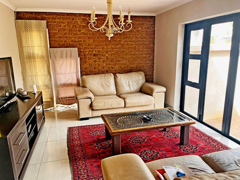 A cozy living room featuring an exposed brick feature wall, polished tile flooring, and direct access to an outdoor area through a glass door.