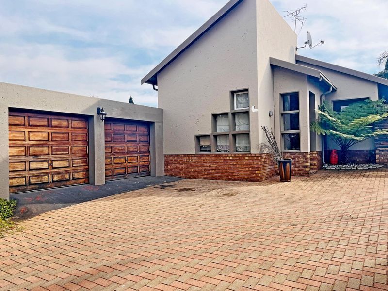 Front elevation of a townhouse featuring a double garage with timber doors, a brick-paved driveway, and a combination of facebrick and plastered wall finishes.