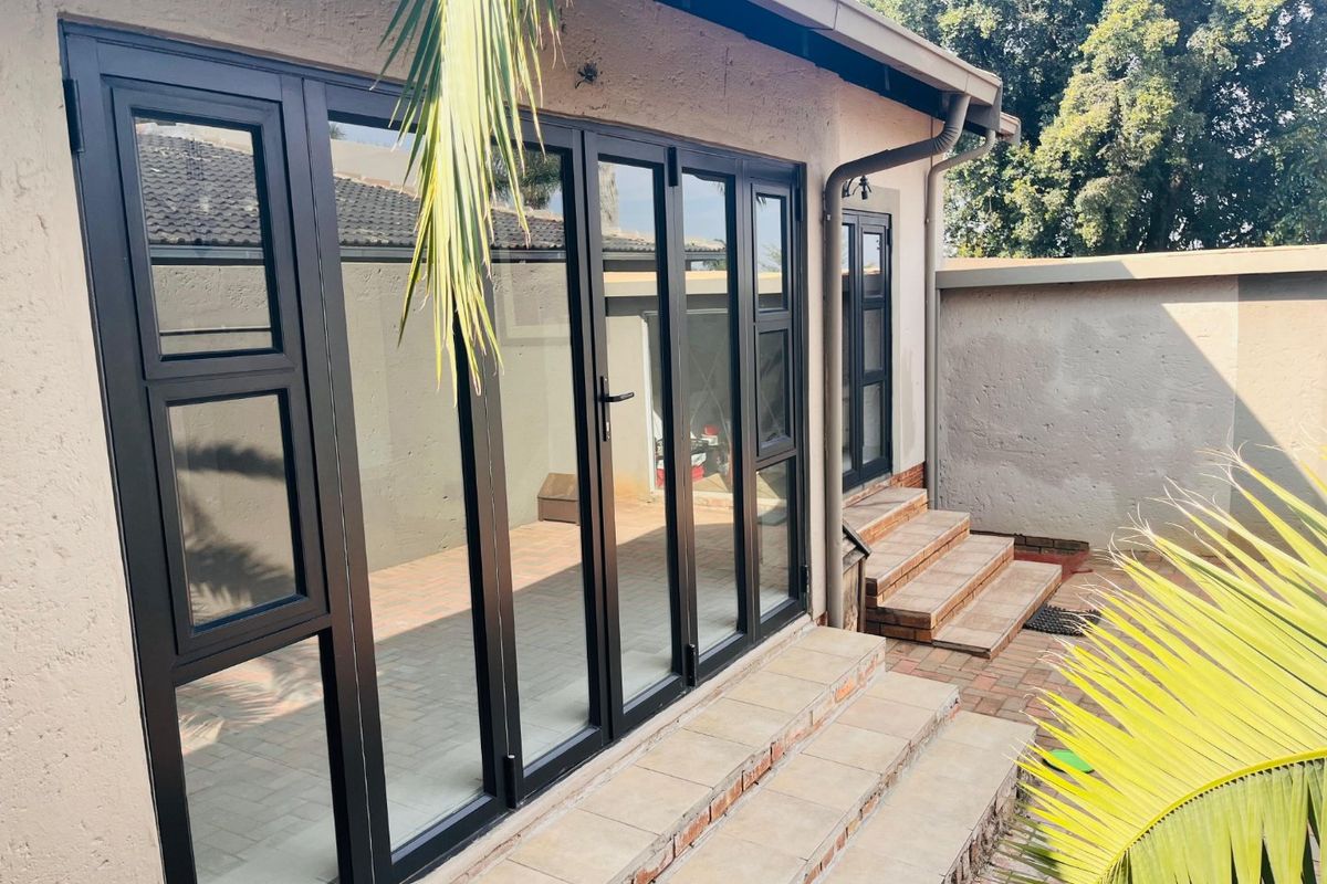 Rear exterior view of the townhouse featuring modern black aluminium stacker doors leading onto a paved patio area with tiled steps.