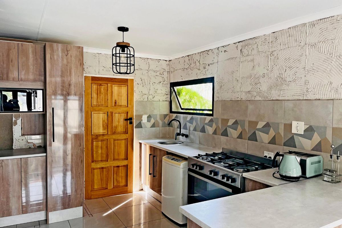 Kitchen featuring wood-look cabinetry, gas stove, oven, and tiled backsplash. The space includes a wooden door and requires finishing on the upper wall section.