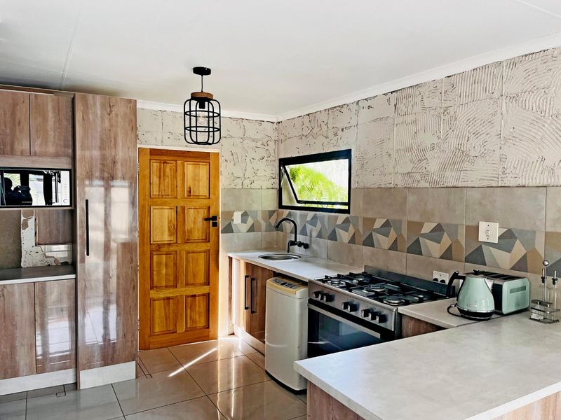 Kitchen featuring wood-look cabinetry, gas stove, oven, and tiled backsplash. The space includes a wooden door and requires finishing on the upper wall section.