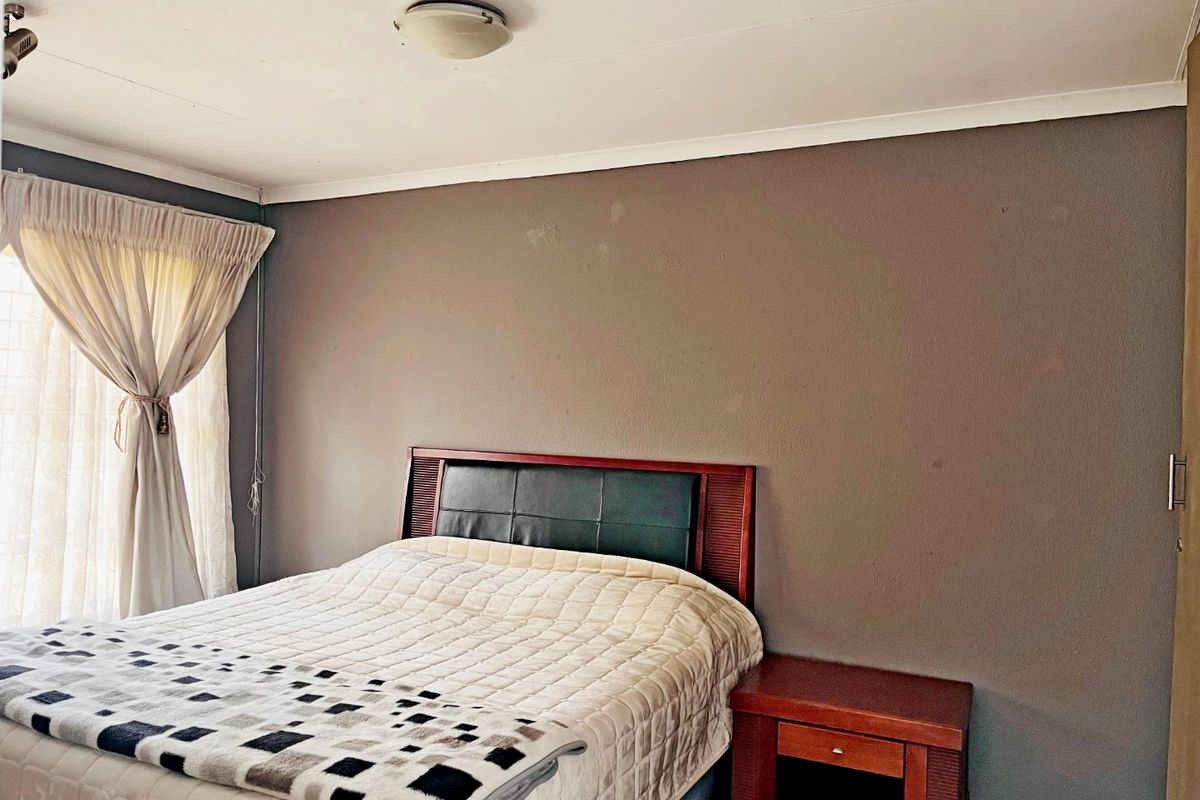 A standard bedroom featuring a neutral grey accent wall, built-in cupboard storage, and a ceiling-mounted light fixture.