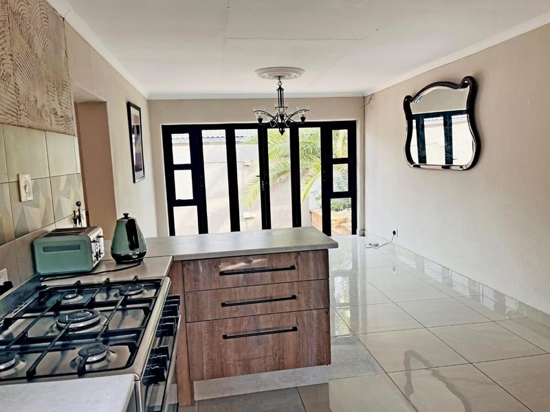 Open-plan kitchen and living area featuring modern wood-finish cabinetry, gas hob, tiled flooring, and large glass doors leading to the outdoor space.