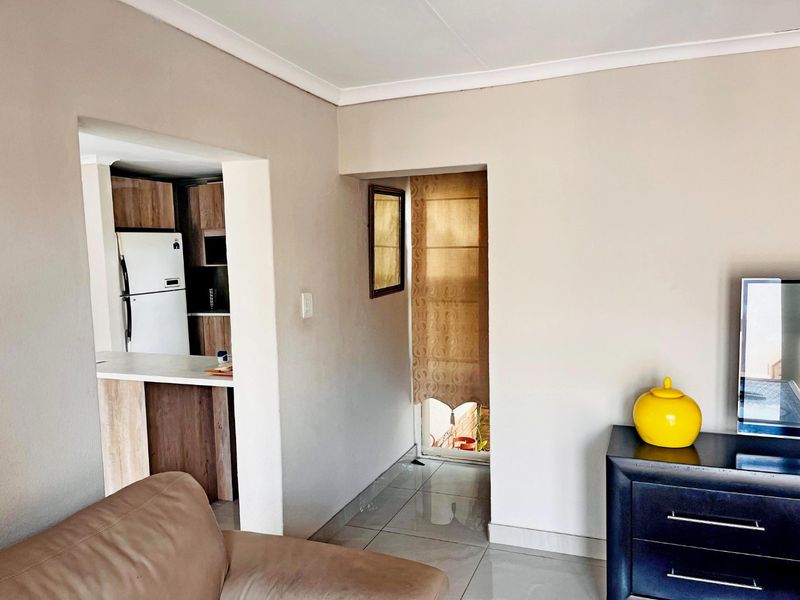 Open plan living area featuring tiled flooring and a view into the adjacent kitchen with built-in cabinetry and countertops.