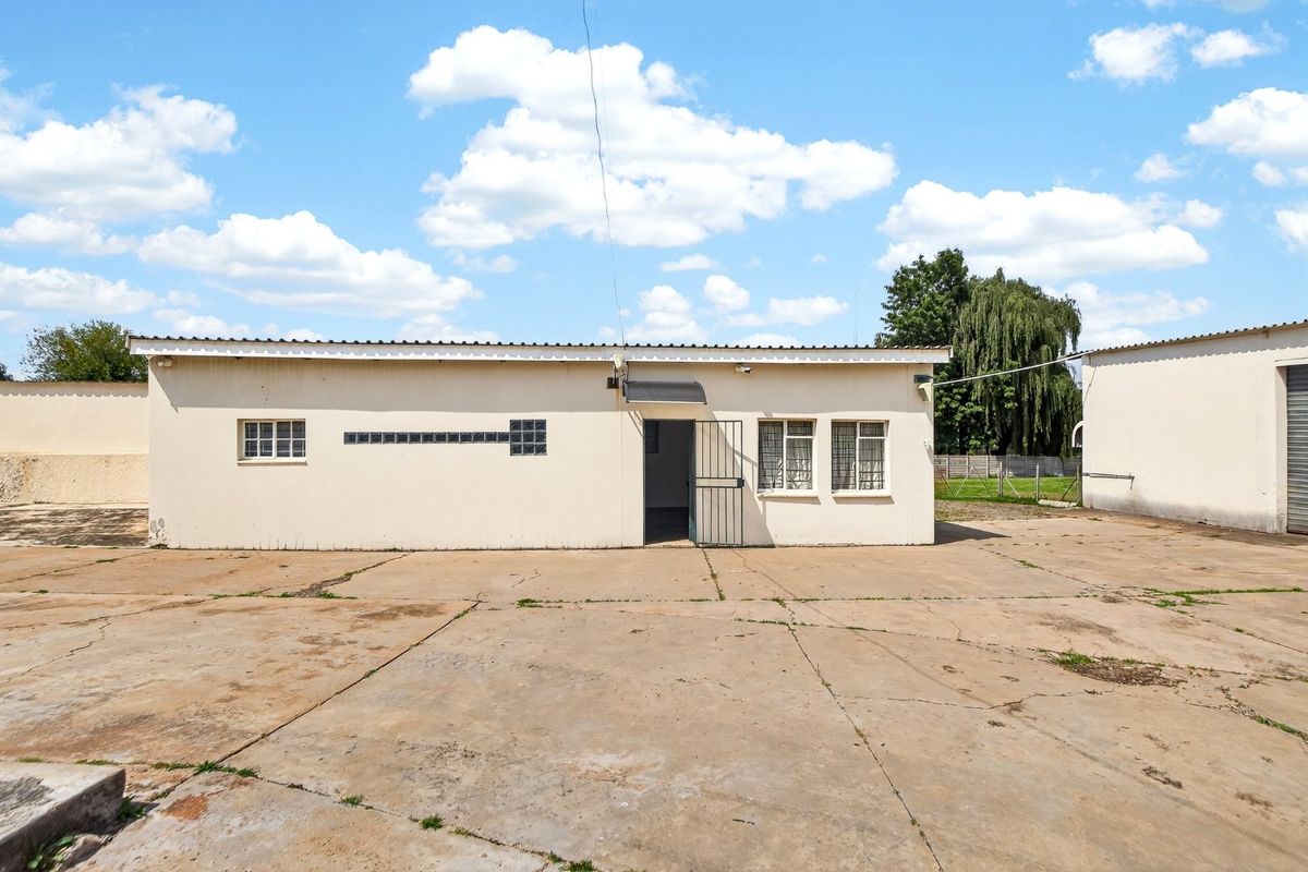Rear exterior view of a farm building featuring a concrete apron, security gate, and basic window fixtures.