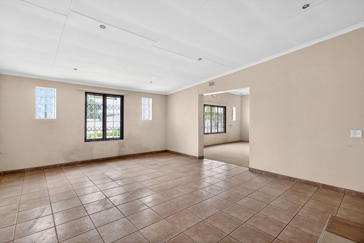 An empty, open-plan living area featuring ceramic floor tiles, security-barred windows, and recessed lighting, requiring minor cosmetic updates to the walls.