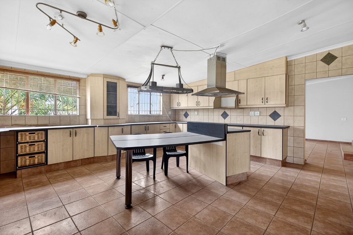 Spacious kitchen featuring laminate cabinetry, tiled splashbacks, a central breakfast bar, and an extractor fan, offering a functional layout with potential for modern updates.