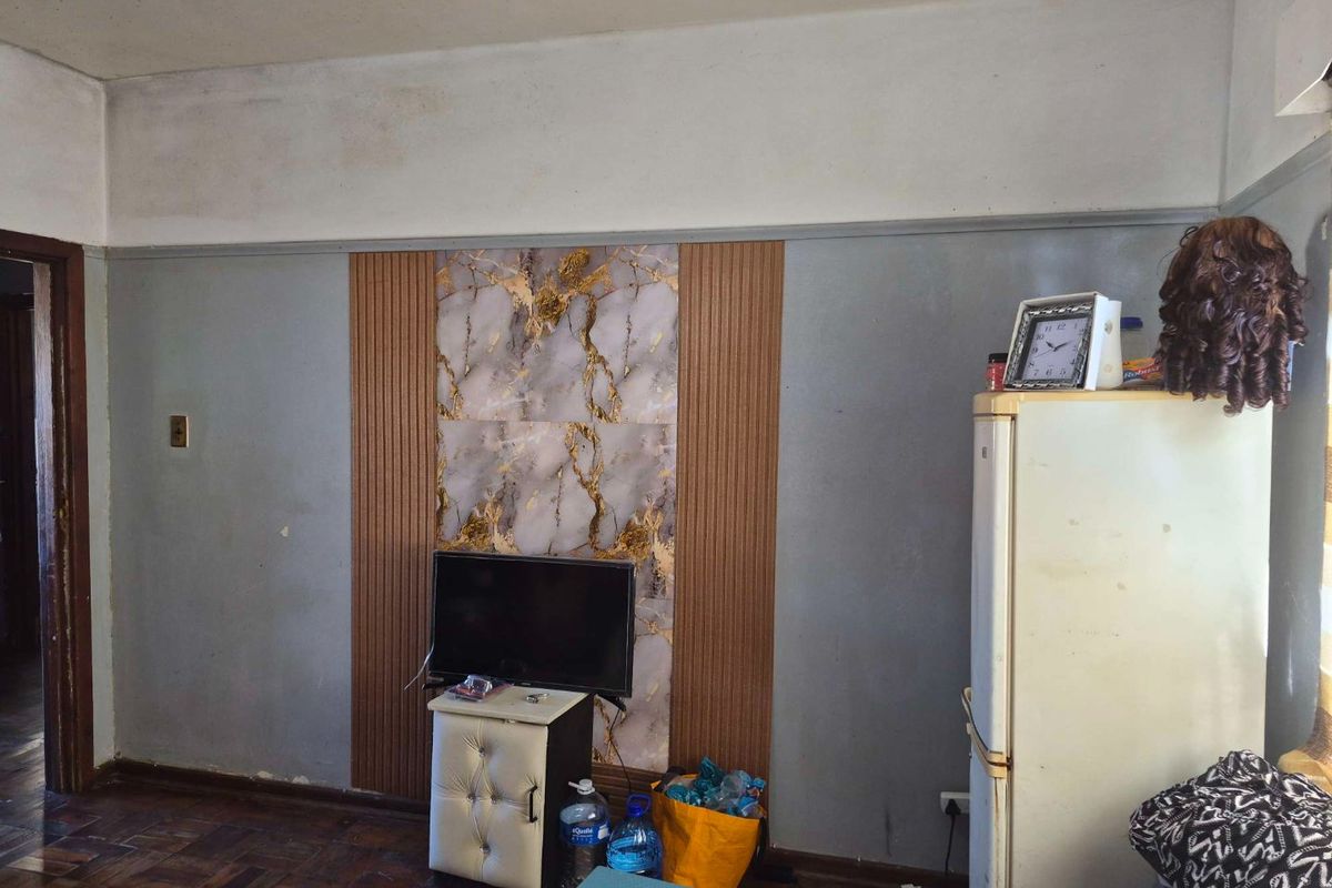 Living area featuring parquet flooring and decorative wall paneling, currently showing signs of wear and requiring cosmetic updates.