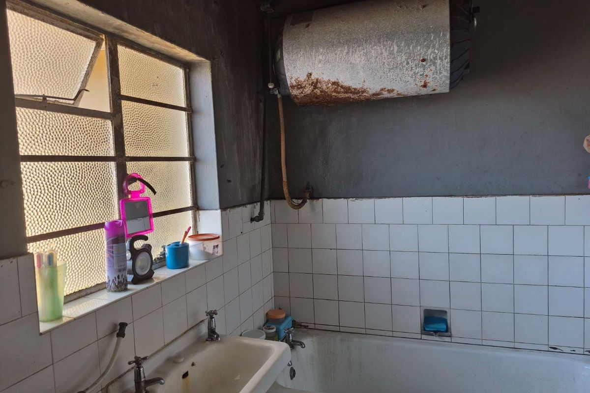 A dated bathroom featuring a bathtub, pedestal basin, and an exposed, corroded electric water heater requiring significant maintenance or replacement.