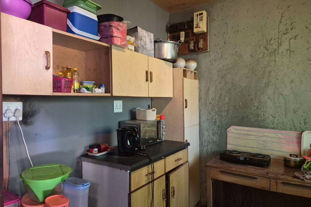 A small kitchen area featuring basic laminate cabinetry and countertop, requiring significant cosmetic updates and maintenance to the wall finishes and electrical fixtures.