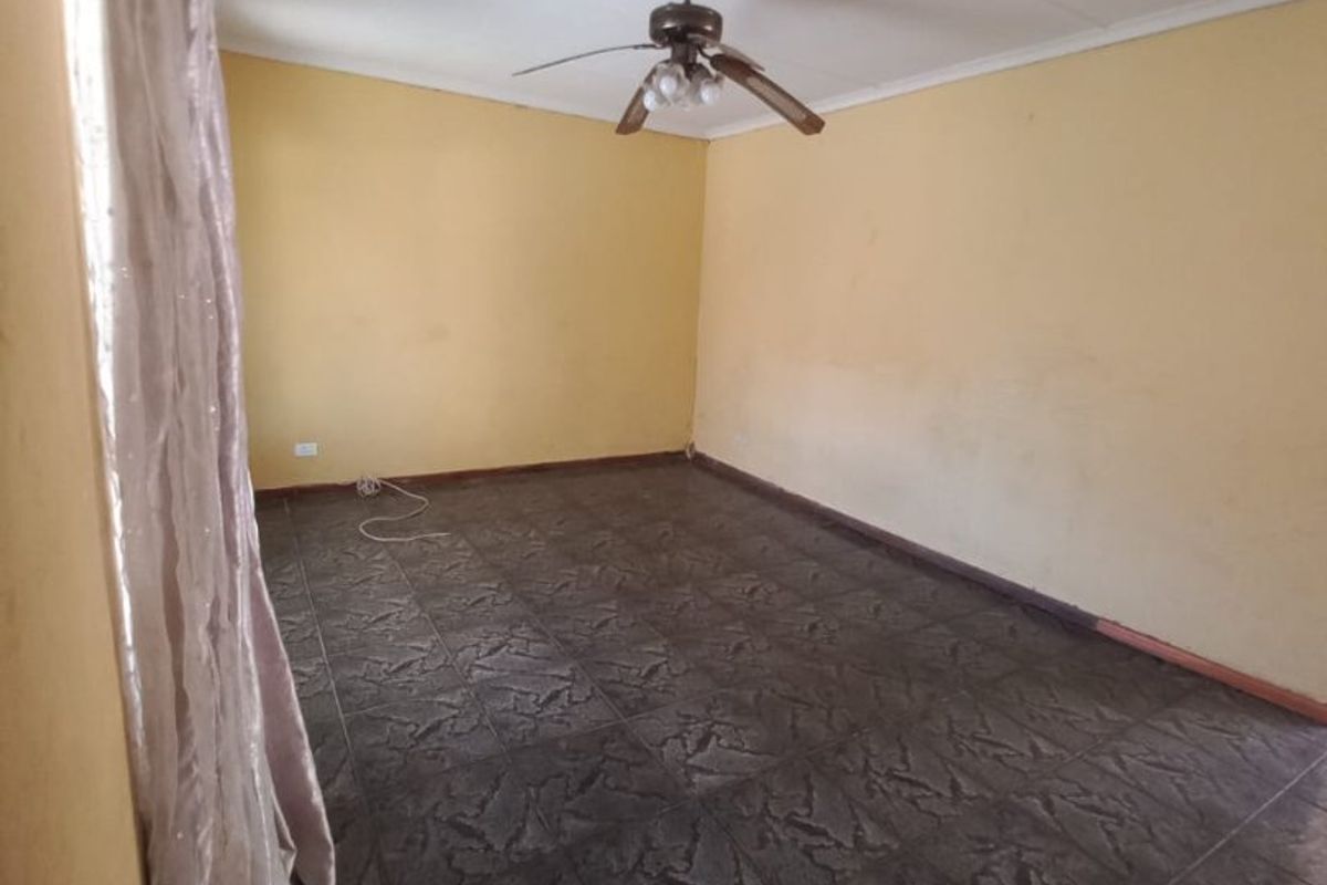 An empty living room featuring dark tiled flooring and a ceiling fan, with yellow walls showing signs of wear.