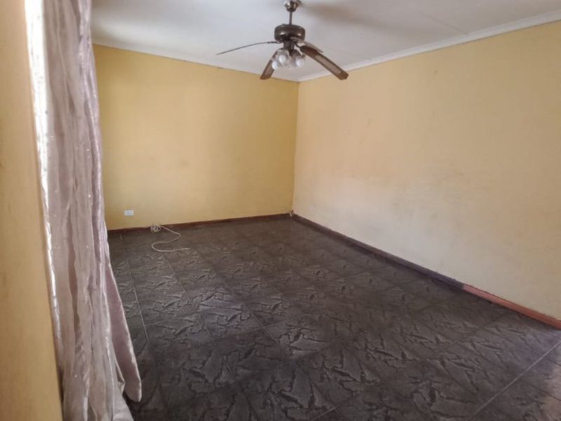 An empty living room featuring dark tiled flooring and a ceiling fan, with yellow walls showing signs of wear.