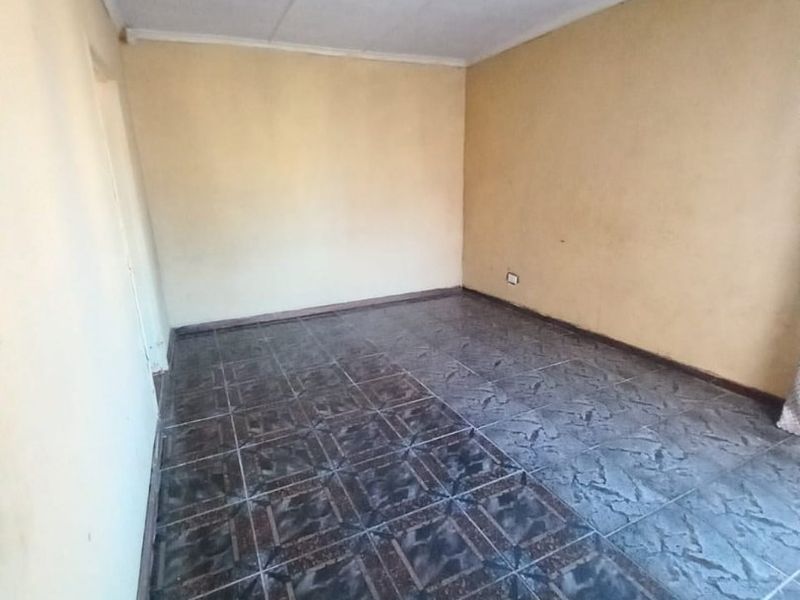 An empty bedroom featuring dark patterned floor tiles and a simple ceiling finish, providing a blank canvas for potential renovation or interior design updates.