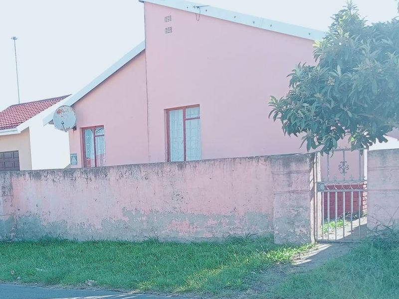 A street-facing view of a residential property featuring a pink exterior wall, metal window frames, and a gated entrance with a boundary wall.