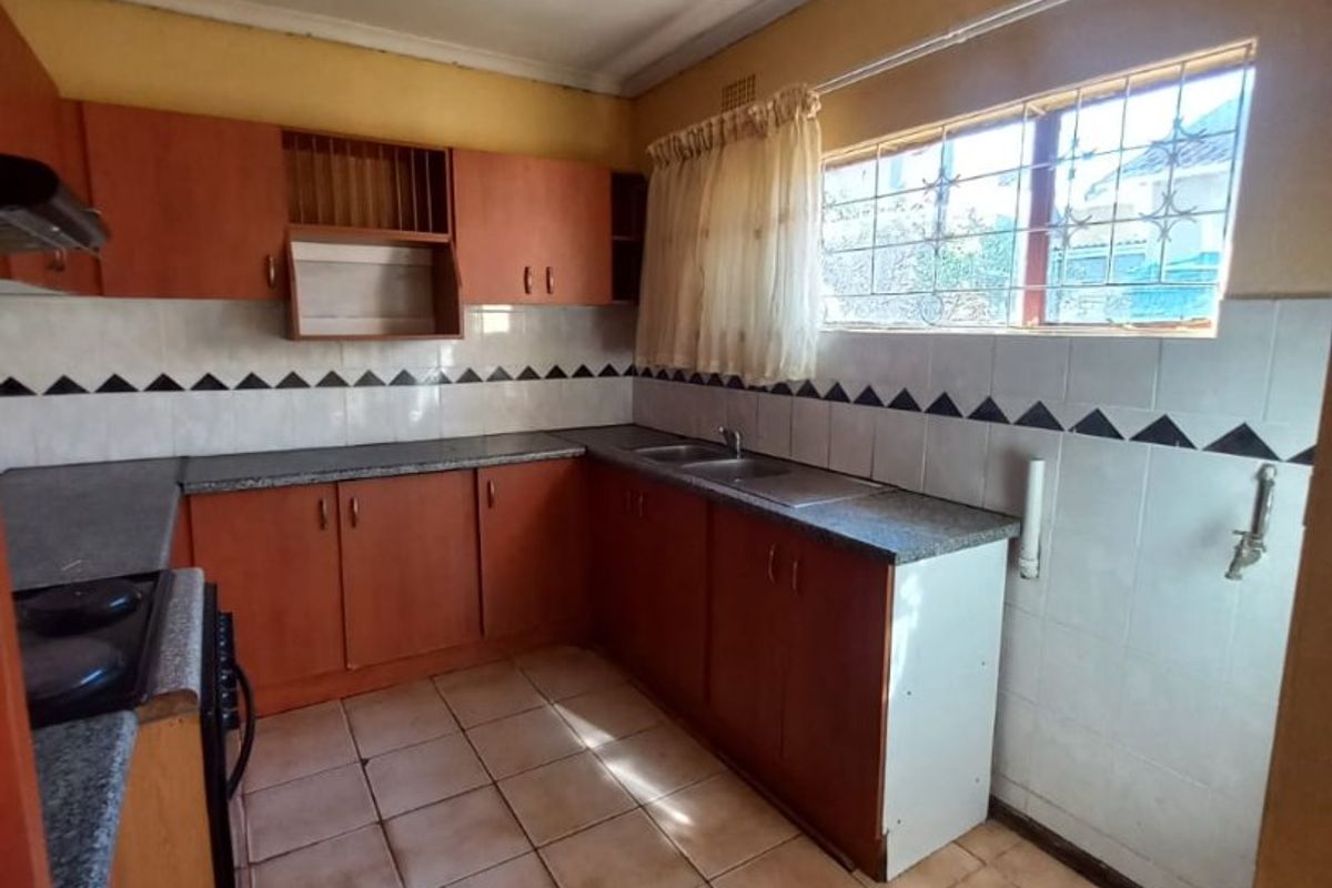 A dated kitchen featuring laminate cabinetry, stone-look countertops, a stainless steel sink, and ceramic tile flooring, offering significant potential for modernization.