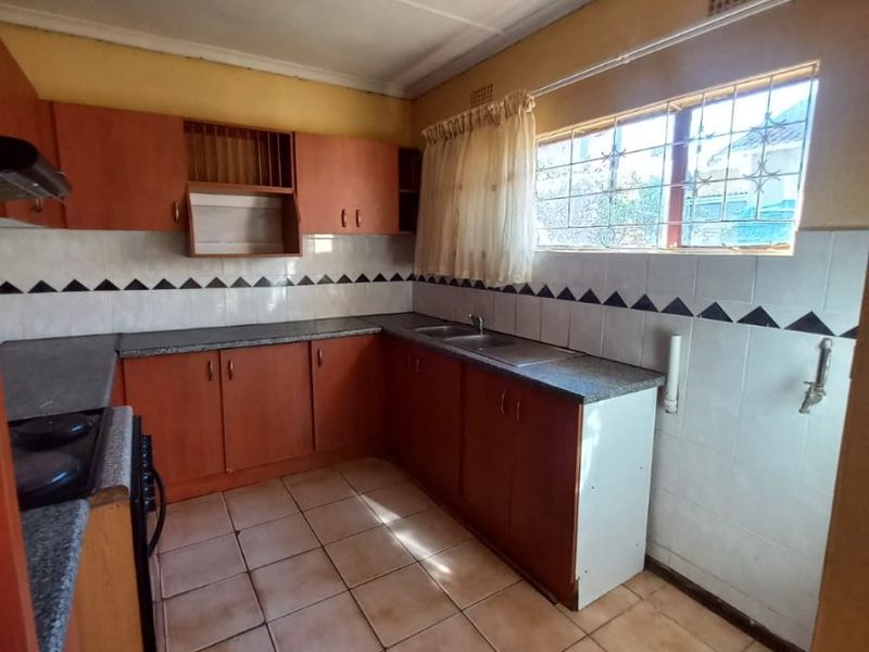 A dated kitchen featuring laminate cabinetry, stone-look countertops, a stainless steel sink, and ceramic tile flooring, offering significant potential for modernization.
