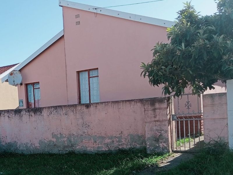 Front view of a residential property featuring a pink exterior wall, a metal pedestrian gate, and a boundary wall showing signs of weathering.