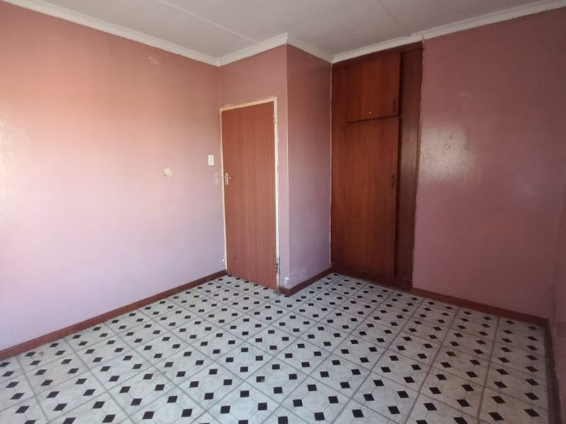 An empty bedroom featuring a built-in wardrobe and patterned vinyl flooring, offering a blank canvas for renovation and interior design updates.