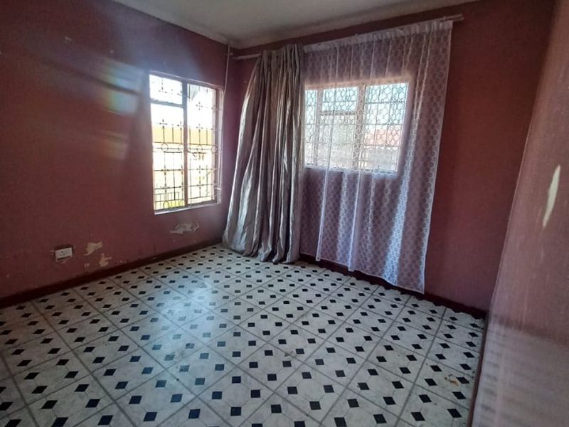 An empty bedroom featuring patterned tiled flooring, security bars on windows, and walls requiring cosmetic attention and repainting.