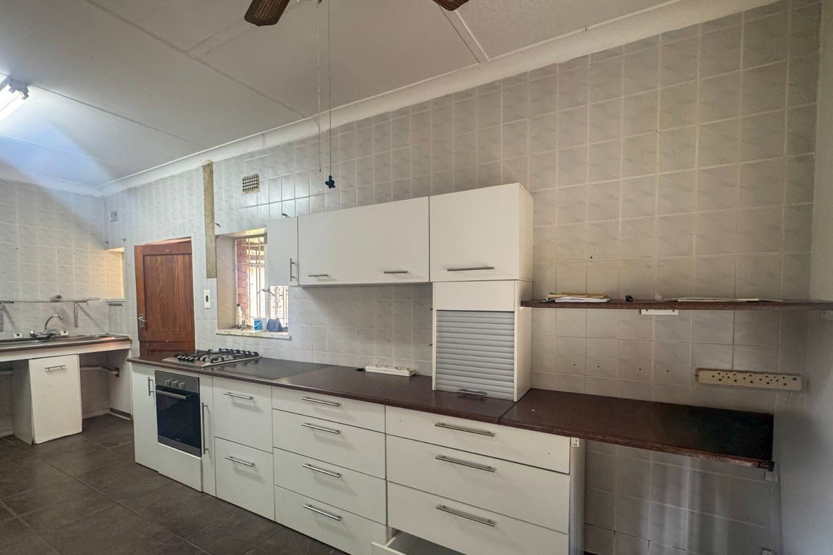 A functional kitchen featuring white cabinetry, a gas hob, built-in oven, and tiled splashbacks, currently vacant and ready for cosmetic updates.