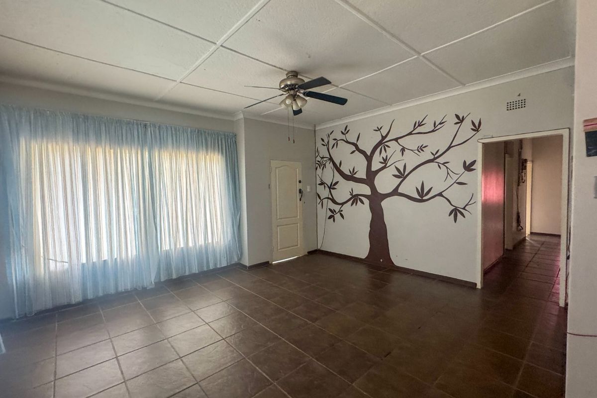 Spacious living area featuring tiled flooring, a ceiling fan, and a decorative wall mural, offering a blank canvas for personalization.