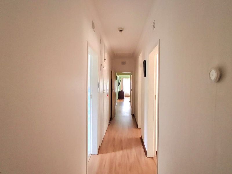 A clean, neutral hallway featuring light-toned laminate flooring and recessed ceiling lighting, providing access to multiple rooms within the home.