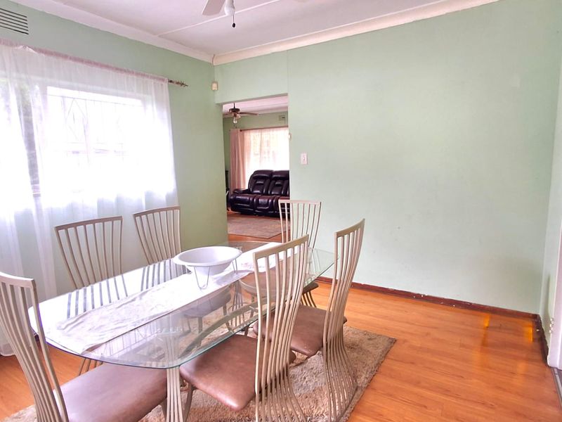 Dining room featuring laminate flooring, coved cornicing, and a ceiling fan, with an open transition to the adjacent living area.