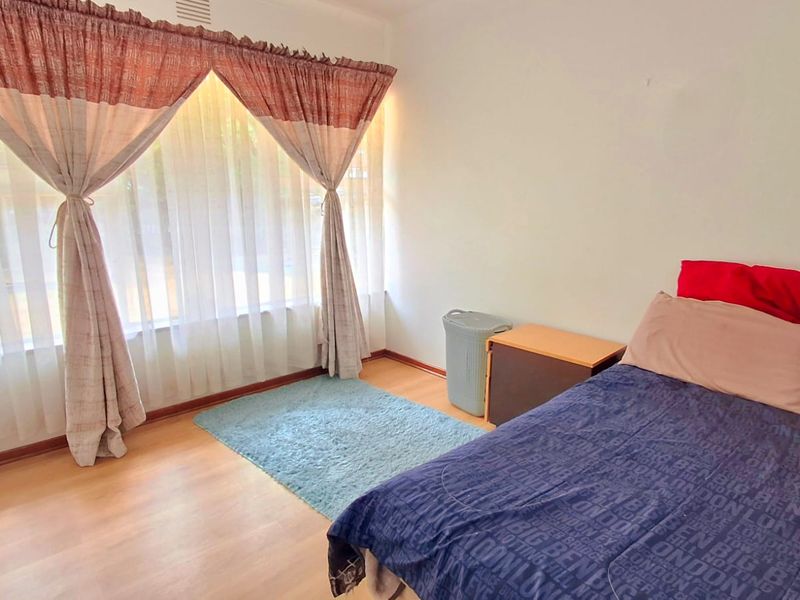 A bedroom featuring laminate flooring and a large window with curtains, providing natural light to the space.