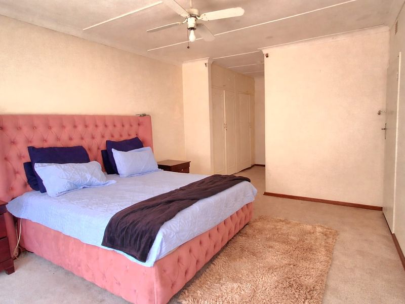 Spacious bedroom featuring built-in cupboards, a ceiling fan, and carpeted flooring, offering a blank canvas for potential updates and modernization.