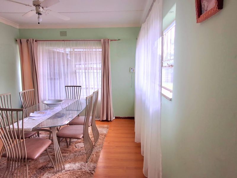 A dining room featuring laminate flooring, a ceiling fan, and large windows with security bars, offering a functional space for family meals.