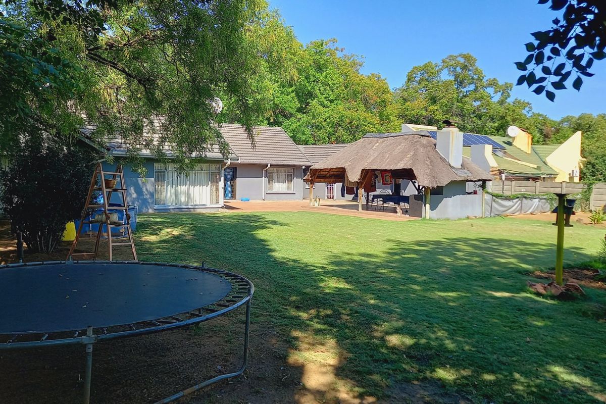 Spacious rear garden featuring a large lawn, a traditional thatched lapa with a built-in braai, and a main house with a tiled roof.